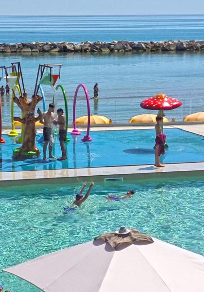 Piscina colorata con giochi d'acqua, scivoli e mare sullo sfondo.