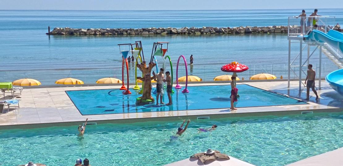 Piscina e giochi d'acqua colorati, mare calmo, giornata estiva gioiosa.