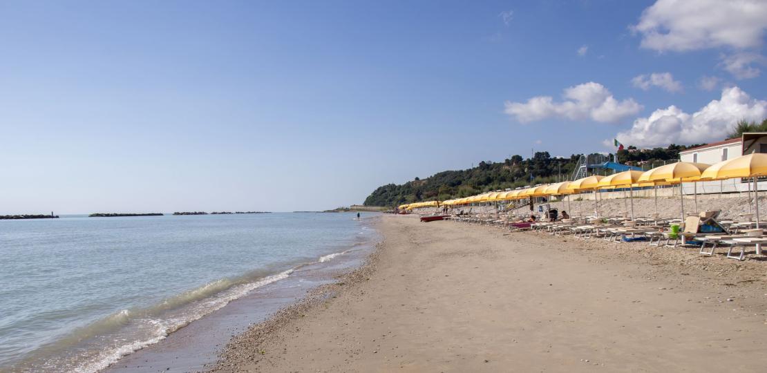 Spiaggia tranquilla con ombrelloni gialli, mare calmo e cielo limpido.