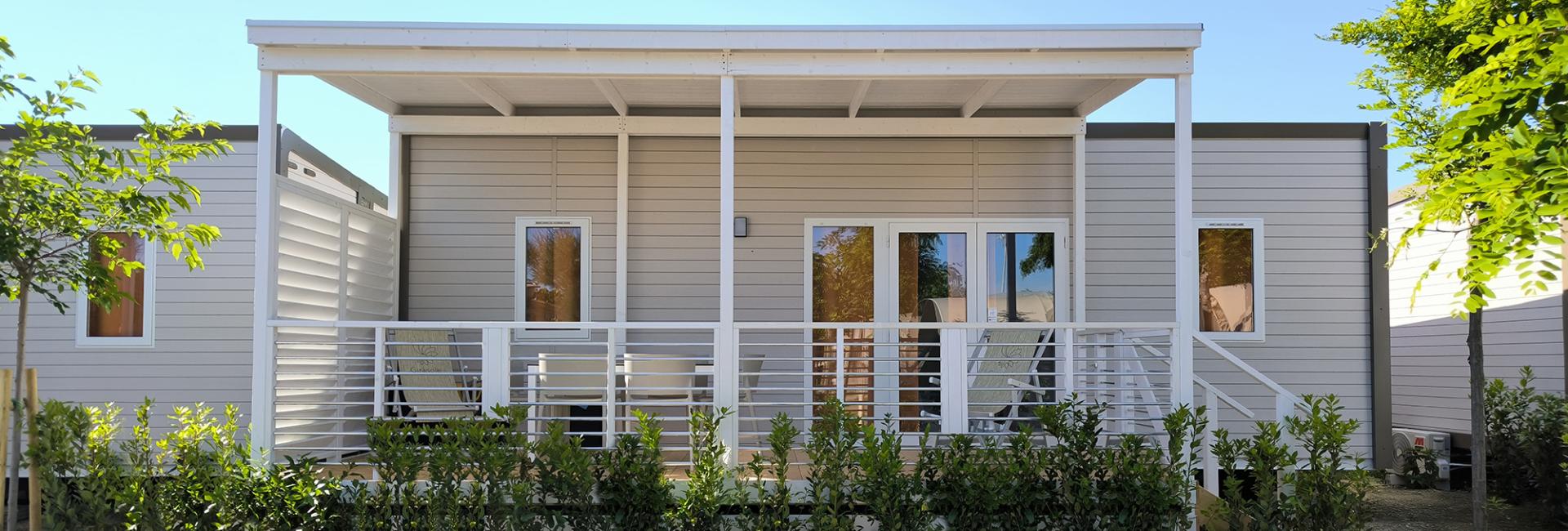Casa mobile moderna con veranda, circondata da verde e cielo limpido.