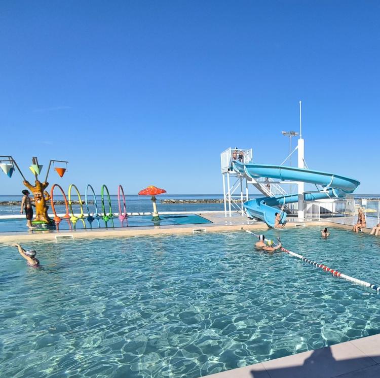Piscina soleggiata, scivolo blu, giochi d'acqua, relax estivo, cielo limpido.