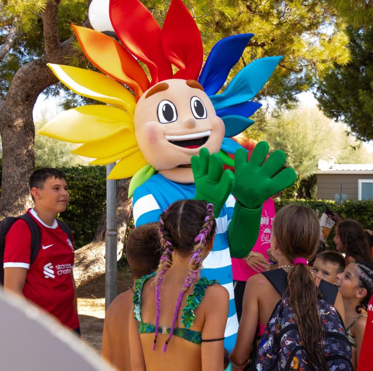 Un colorato personaggio felice circondato da bambini sorridenti in un parco.