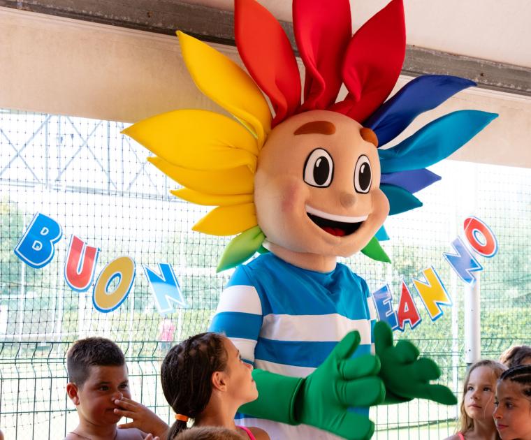 Festa di compleanno colorata con mascotte sorridente e bambini felici.