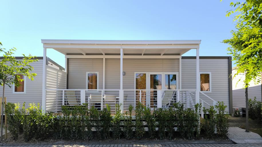 Casa mobile moderna con veranda, circondata da verde e cielo limpido.