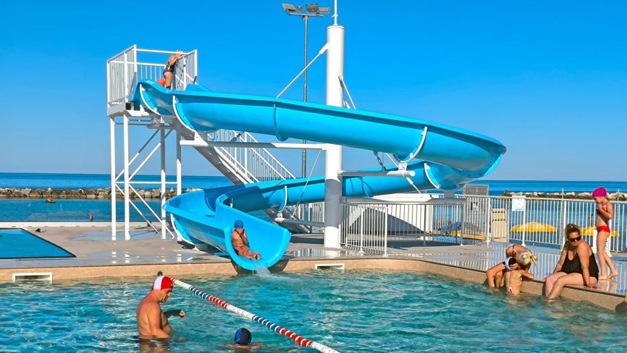 Piscina con scivolo, bambini felici e cielo azzurro.