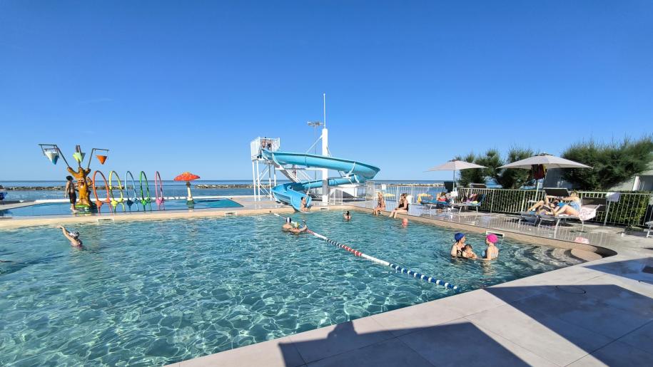 Piscina soleggiata, scivolo blu, giochi d'acqua, relax estivo, cielo limpido.