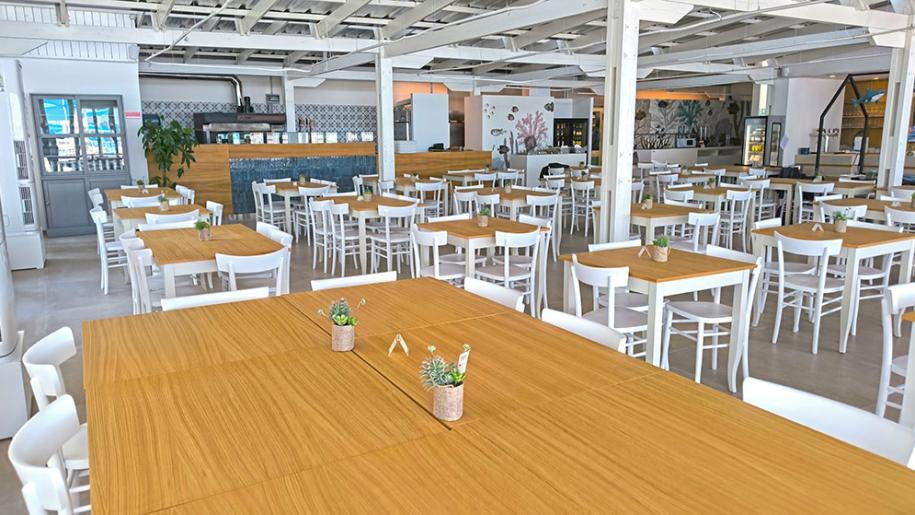 Ampia sala luminosa, tavoli in legno, sedie bianche, atmosfera accogliente e moderna.